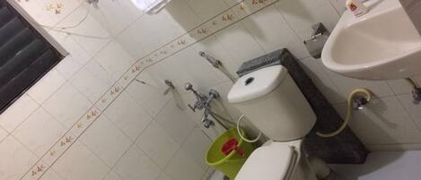 A bathroom with a toilet, bidet, and sink. There are towels hanging on the wall and a green bucket with a red object.