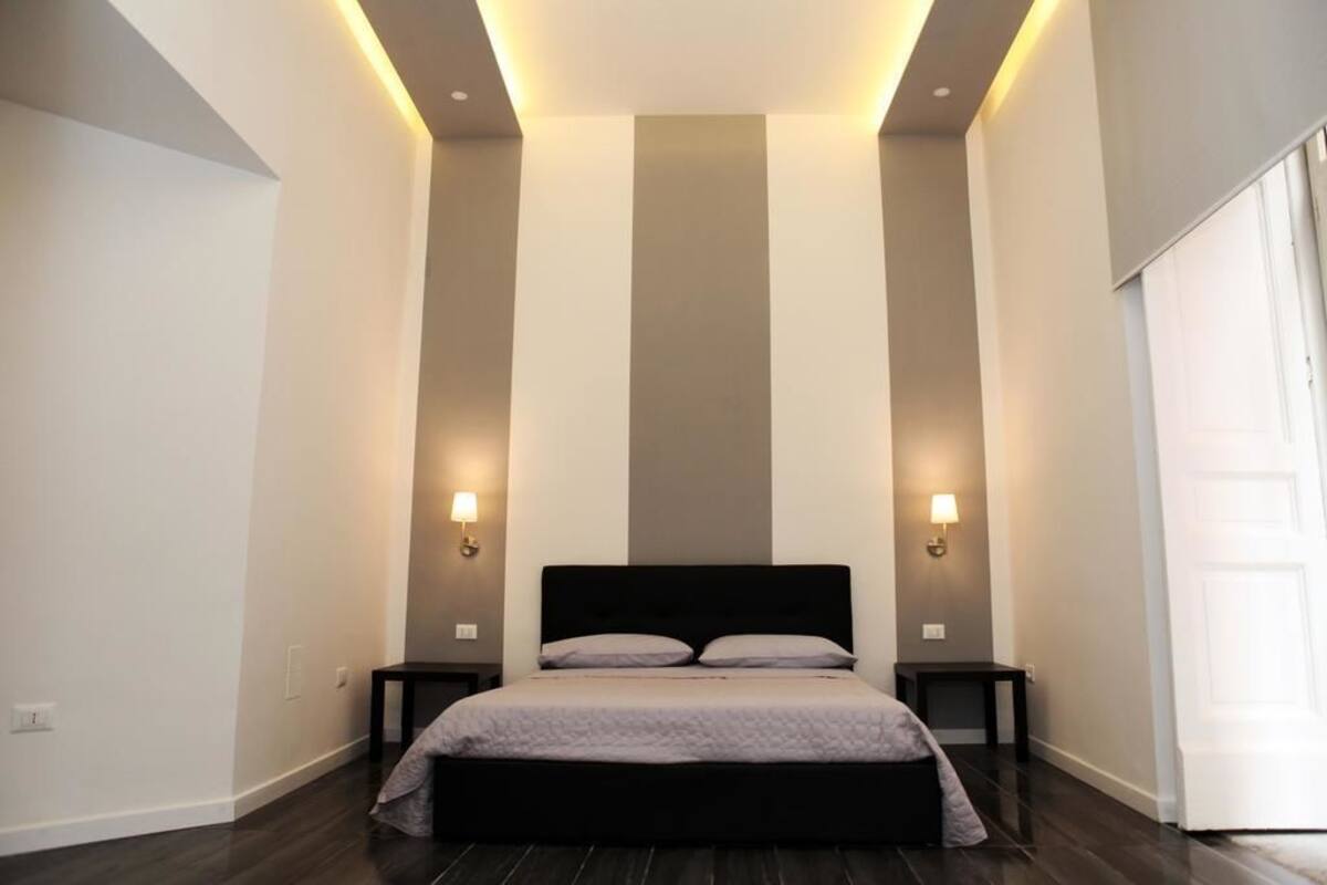 A bedroom with a large bed, two bedside tables, and wall-mounted lighting.