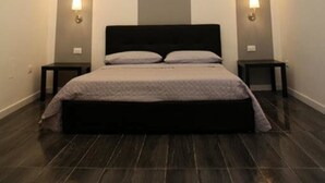 A modern bedroom with a bed centered under a recessed ceiling light, flanked by two bedside tables with lamps. - Maison Arena (Naples)
