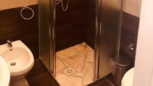 A small, enclosed shower stall with a glass door, a handheld showerhead, and a wall-mounted faucet. - Maison Arena (Naples)