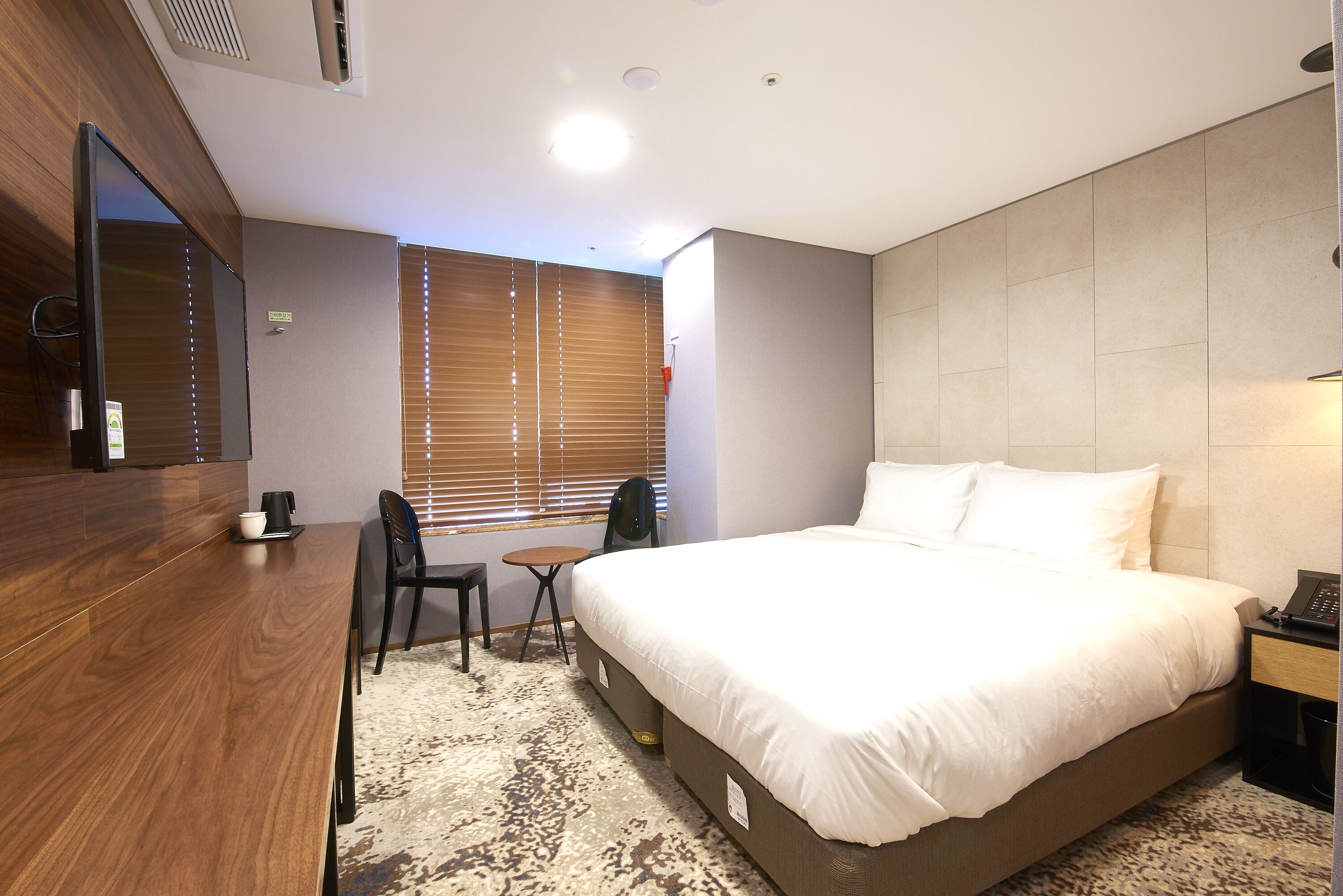 A hotel room with a large bed, a desk, a chair, and a small table.