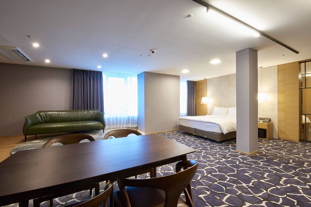 A hotel room with a dining table, a green sofa, a bed, and a patterned carpet.