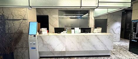 A hotel reception desk with a self-check-in kiosk, a marble counter, and a digital display.