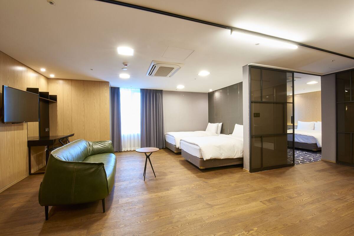 A hotel room with a green sofa, a bed, a small table, and a TV on the wall.