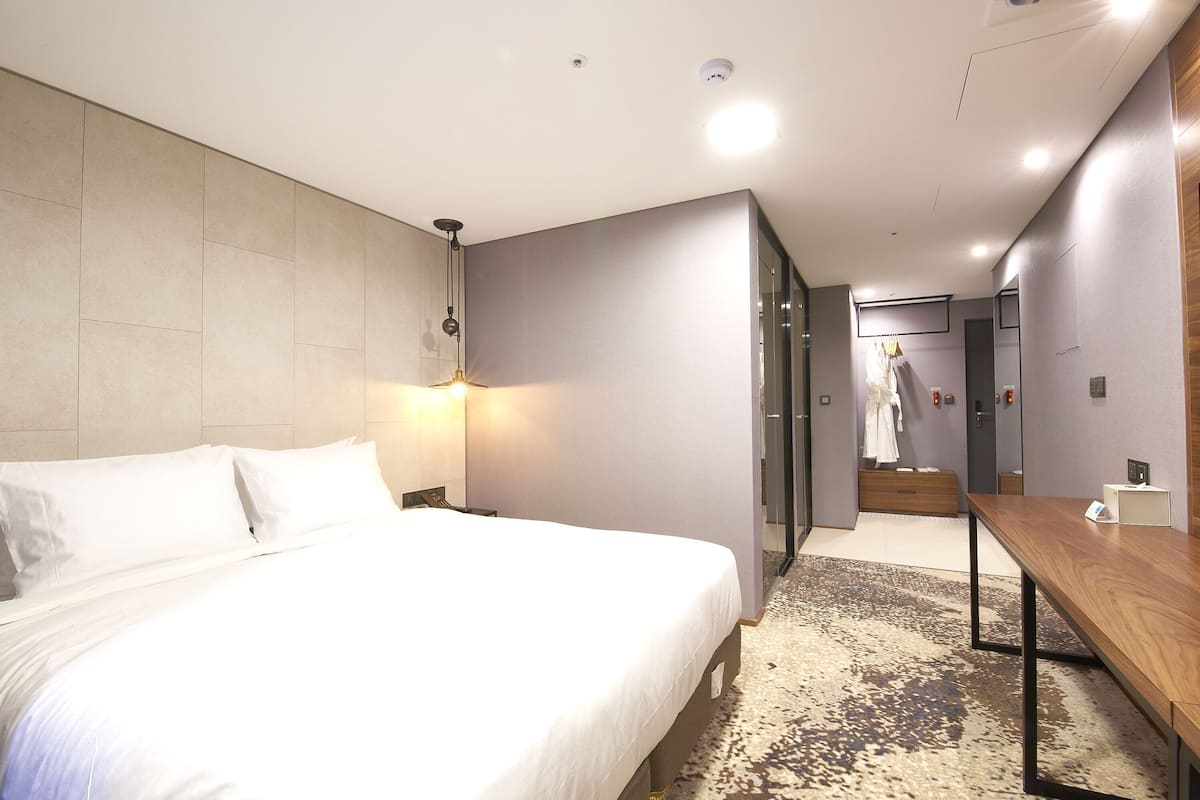 A modern hotel room with a large bed, a wooden desk, and a walk-in closet.