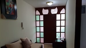 A living room with a sofa, a patterned pillow, a wall-mounted phone, and a door with decorative glass panels. - Guayaquil In Love (Guayaquil)