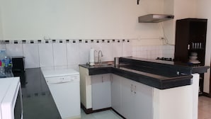 A compact kitchen with white cabinets, a black countertop, a built-in stove, and a water dispenser. - Guayaquil In Love (Guayaquil)