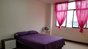 A bedroom with a bed, a nightstand, a fan, and a window with sheer curtains. - Guayaquil In Love (Guayaquil)
