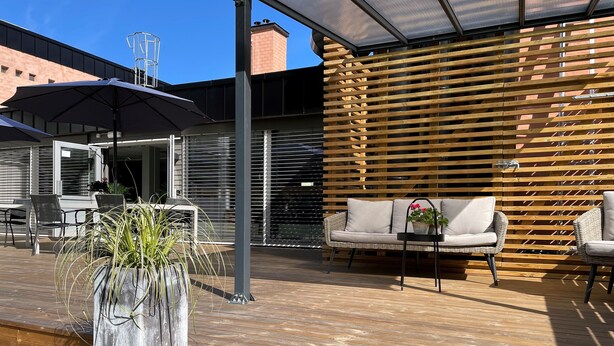 An outdoor patio with a wooden deck, a cushioned sofa, a small table, and a potted plant. - Emma Gjestehus (Bærum)