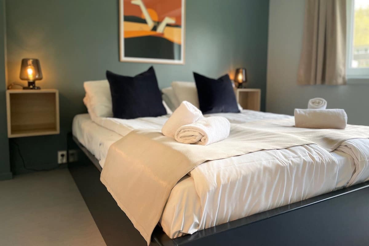 A neatly made bed with a white comforter and pillows, two bedside lamps, and a framed artwork on the wall.
