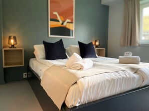 A neatly made bed with a white comforter and pillows, two bedside lamps, and a framed artwork on the wall.