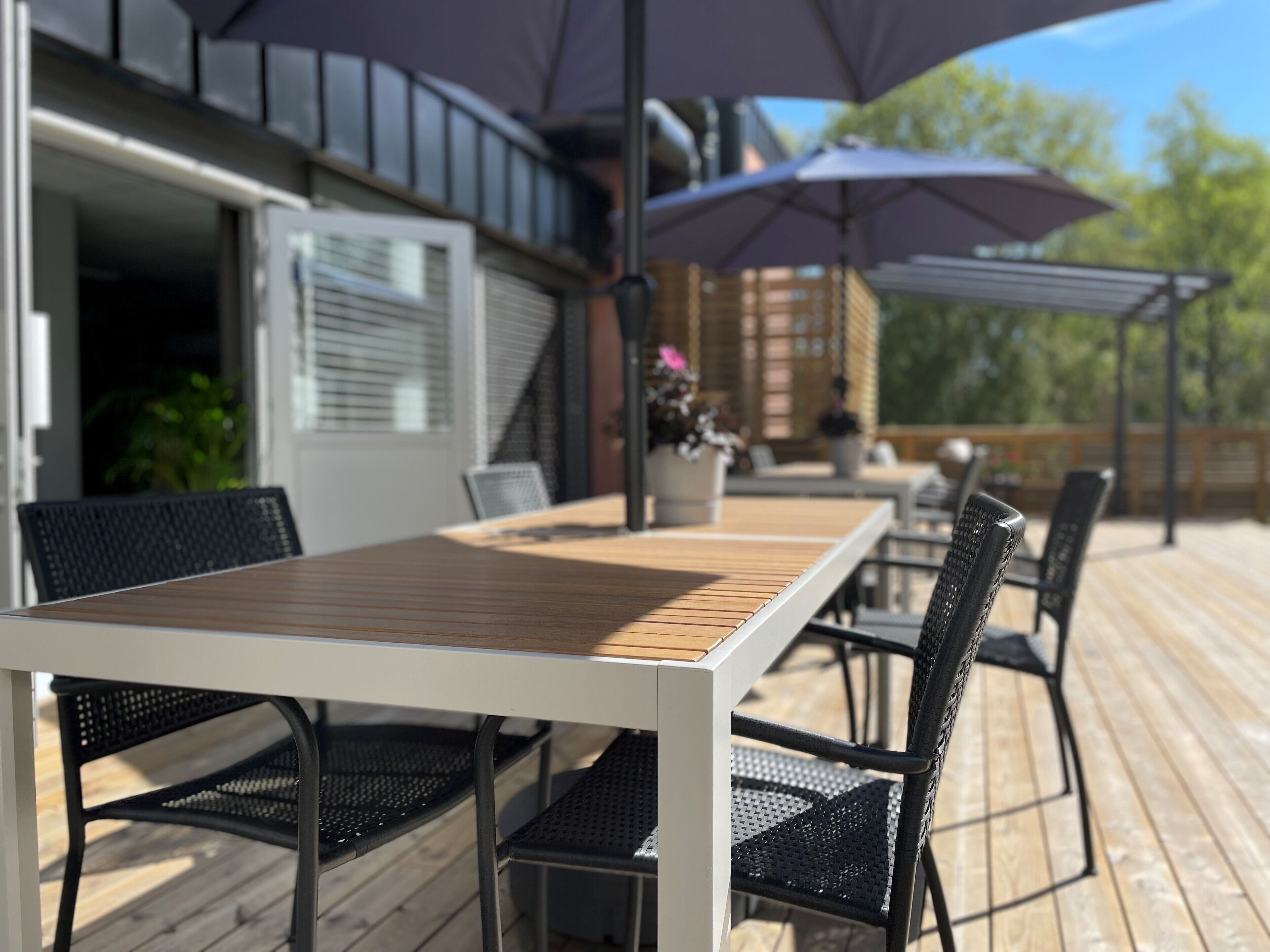 An outdoor patio with a wooden table and black metal chairs, surrounded by umbrellas.