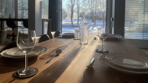 A dining table set with wine glasses, plates, and cutlery in a room with large windows and a view of a snowy landscape. - Emma Gjestehus (Bærum)