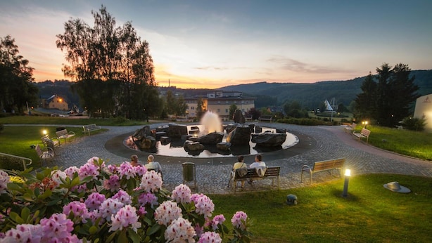 A circular stone fountain surrounded by benches and a well-maintained garden with flowering shrubs. - Kurhotel Bad Schlema (Aue-Bad Schlema)