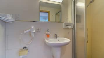 Un baño con lavamanos blanco, espejo, toallero, cabezal de ducha de mano y cabina de ducha con paredes de vidrio.