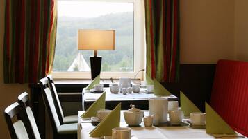 Un comedor con una mesa dispuesta para dos, una lámpara y vistas a un bosque por la ventana.