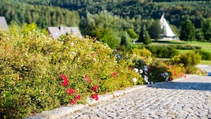 A cobblestone pathway leading through a garden with flowering bushes and a sailboat in the background. - Kurhotel Bad Schlema (Aue-Bad Schlema)