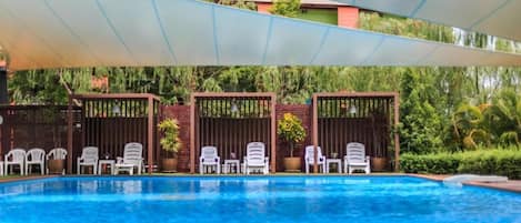 A swimming pool with white lounge chairs and a shaded area.