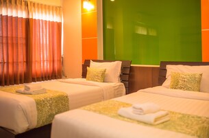 Habitación de hotel con dos camas, cada una con cubrecama verde estampado y almohadas blancas. Presenta una pared de acento verde y una ventana con cortinas naranjas.