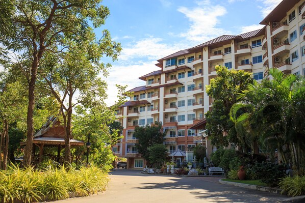 A multi-story hotel with balconies, surrounded by lush greenery and a gazebo.