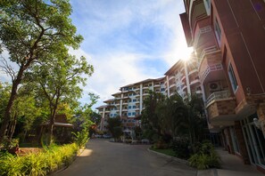A multi-story hotel with a central courtyard, surrounded by lush greenery and a clear sky.