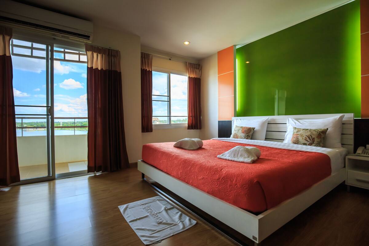 Quarto de hotel com uma cama grande, uma parede verde decorativa e vista para o exterior.