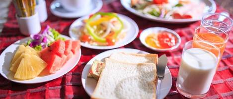Desayuno con platos de fruta, tostadas y leche, además de una taza de café sobre un mantel a cuadros rojos.