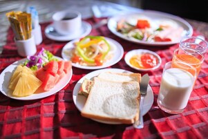 Desayuno con platos de fruta, tostadas y leche, además de una taza de café sobre un mantel a cuadros rojos.