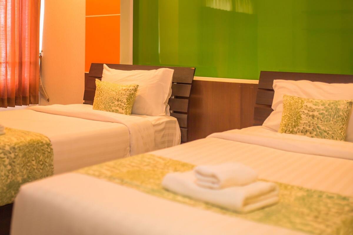 Quarto de hotel com duas camas, cada uma com travesseiro e toalha dobrada.