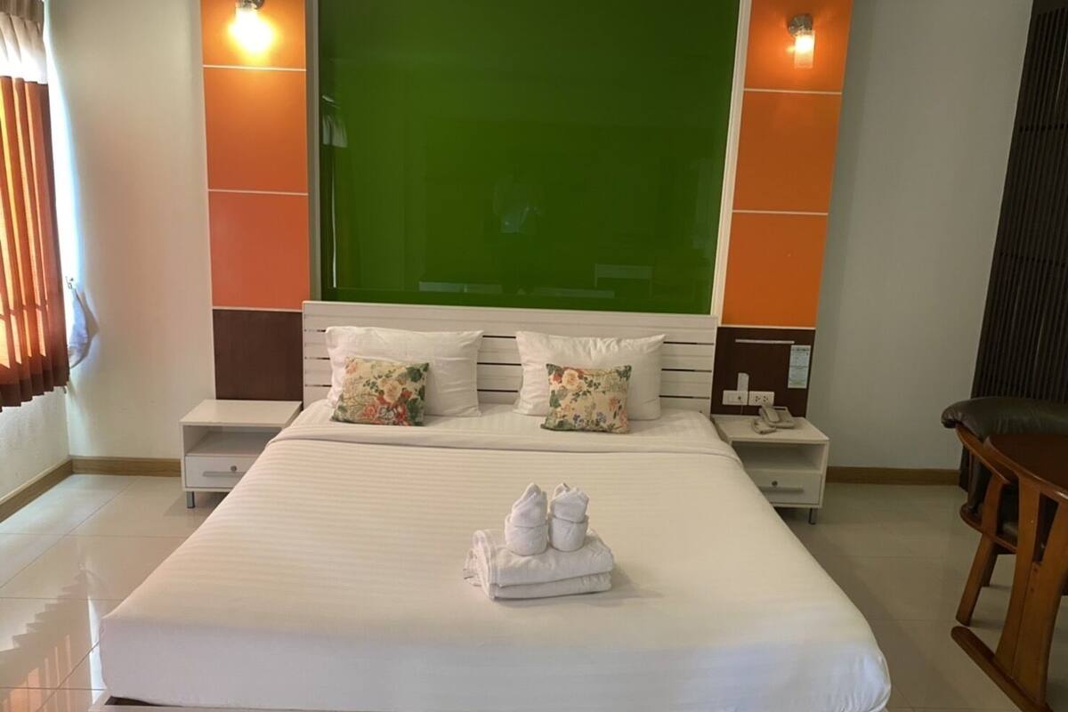 Quarto de hotel com uma cama grande, duas mesas de cabeceira, uma cadeira de madeira e uma parede verde decorativa.