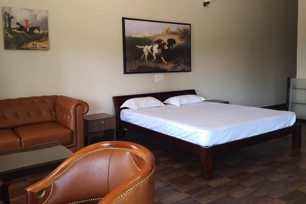 Una habitación con una cama, un sofá de cuero y una silla. Hay dos cuadros en la pared.