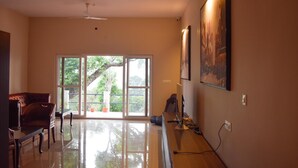 A spacious room with a large window, a ceiling fan, and a desk with a computer. - Forestdale Coorg (Virajpet)