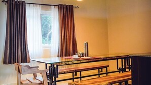 A modern kitchen with a wooden table, bench seating, pendant lights, and a window with curtains. - Forestdale Coorg (Virajpet)