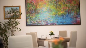 A dining area with a table set for four, a painting of a colorful forest scene, and a potted plant to the left. - Cannatella's Mansion (Palermo)
