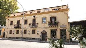 A two-story building with a yellow facade, multiple balconies with flower boxes, and a sign indicating a restaurant. - Cannatella's Mansion (Palermo)
