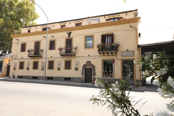 A two-story building with a yellow facade, multiple balconies with flower boxes, and a sign indicating a restaurant. - Cannatella's Mansion (Palermo)