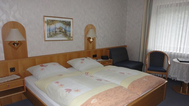 A hotel room with a double bed, two bedside tables with lamps, a chair, a small table, and a painting on the wall. - Pension Haus Volkesbach (Hallenberg)