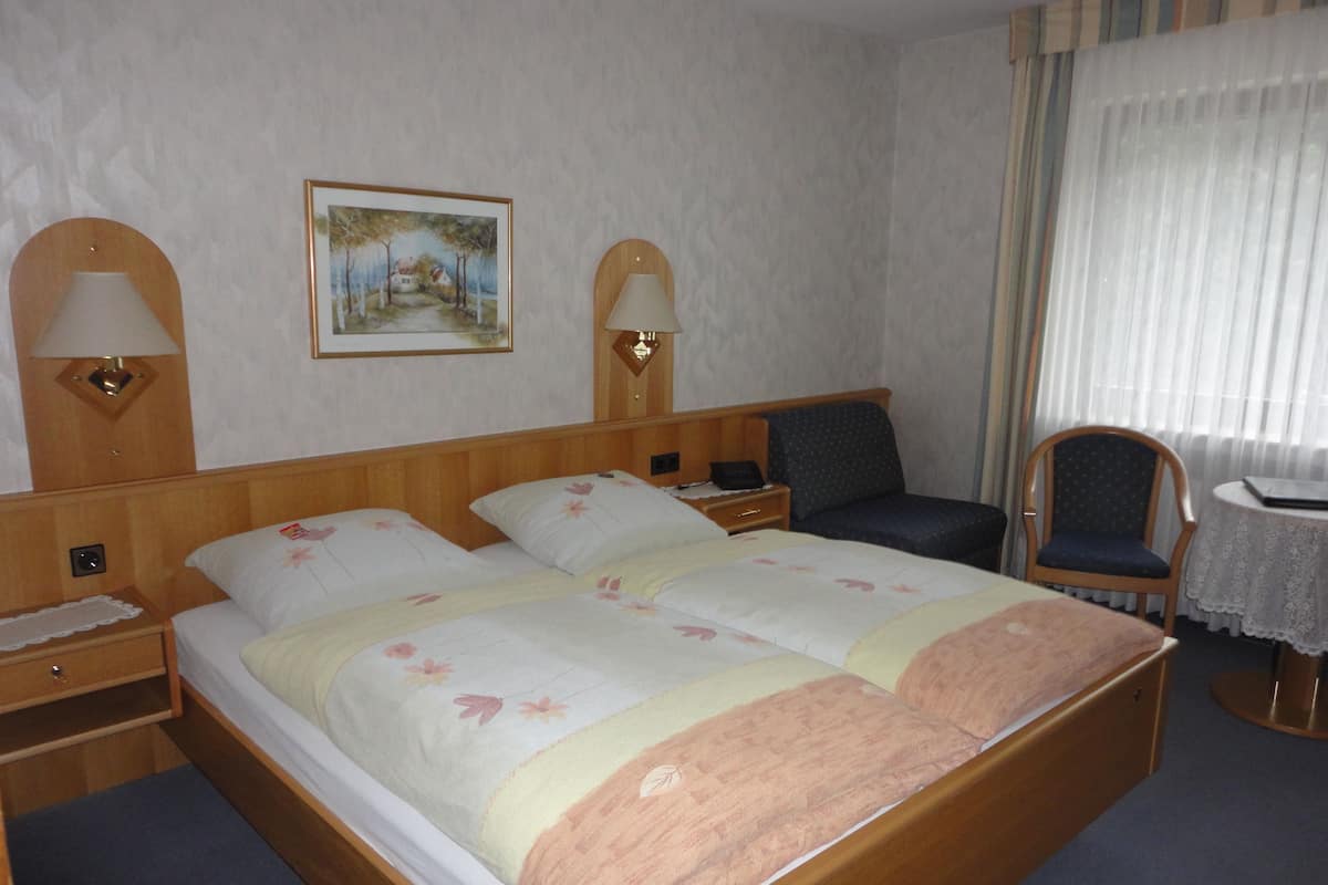Ein Hotelzimmer mit Doppelbett, zwei Nachttischen mit Lampen, einem Sessel, einem kleinen Tisch und einem Bild an der Wand.