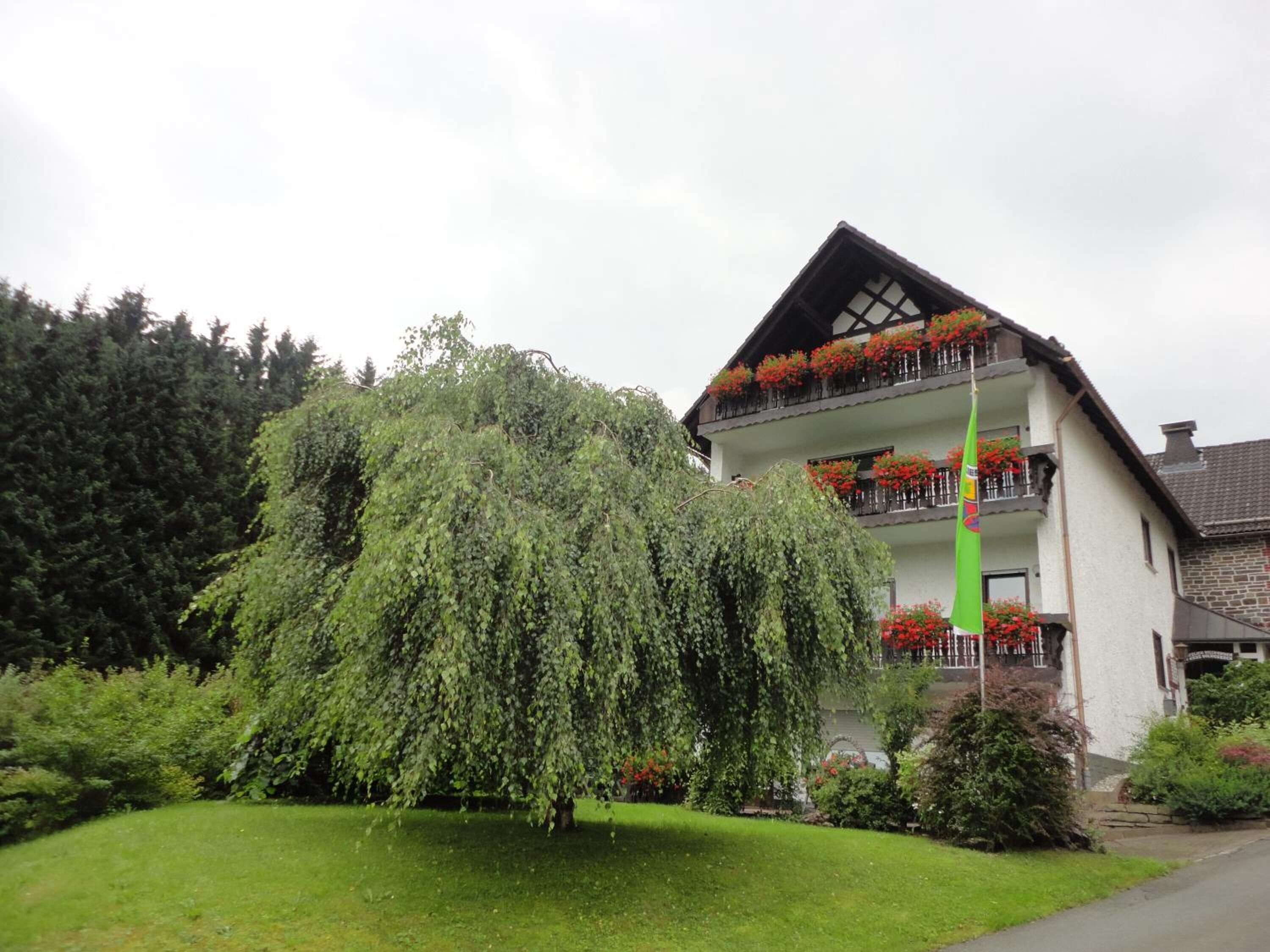 A two-story building with a sloped roof, balconies with flower boxes, and a flagpole.