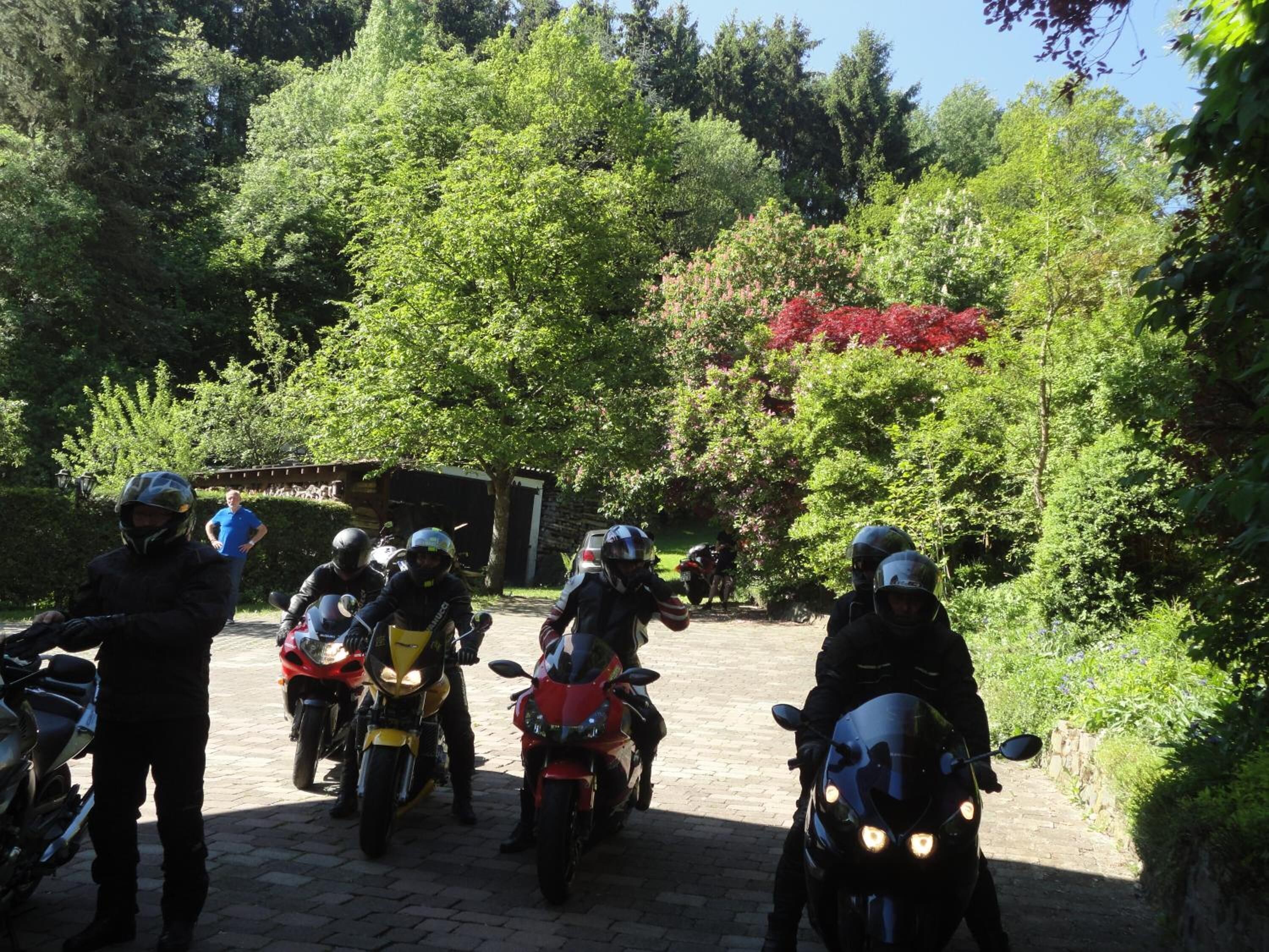 A group of motorcyclists on a paved path surrounded by lush greenery and trees.
