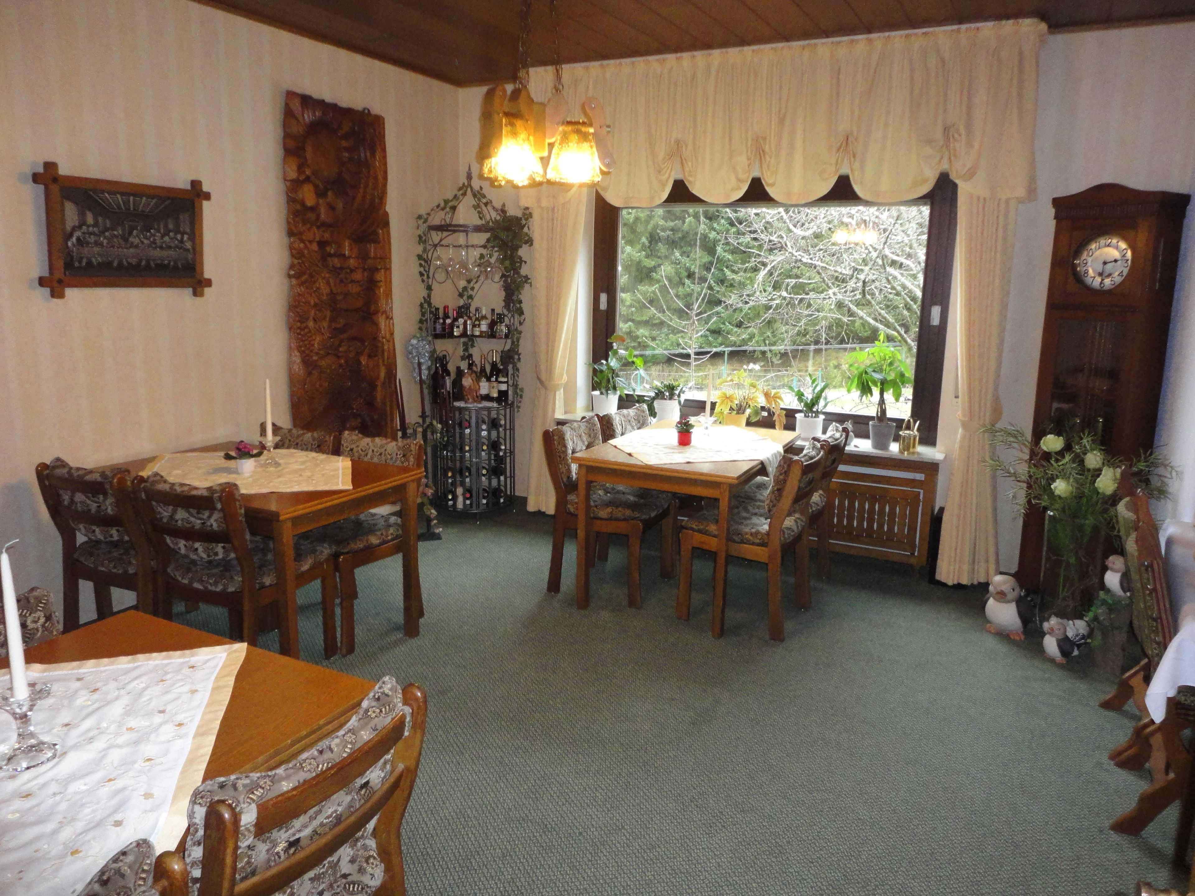 A dining area with a wooden table and chairs, a wine rack, and a view through a window.