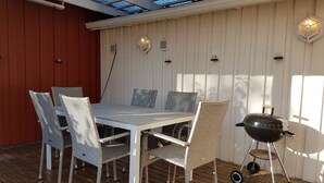 A covered outdoor dining area with a table and chairs, a grill, and a skylight.