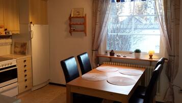 A compact kitchen with a refrigerator, stove, and cabinets. There is a dining table with chairs and a window with curtains.