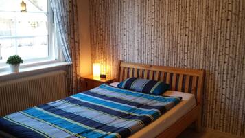 A bedroom with a wooden bed, striped bedding, a bedside lamp, a radiator, and a window with curtains.