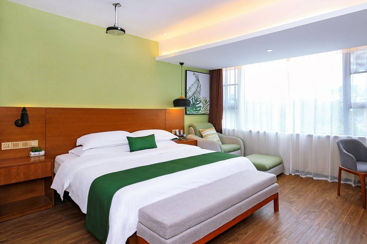 Una habitación de hotel con cama, mesita de noche, silla y un ventanal grande.