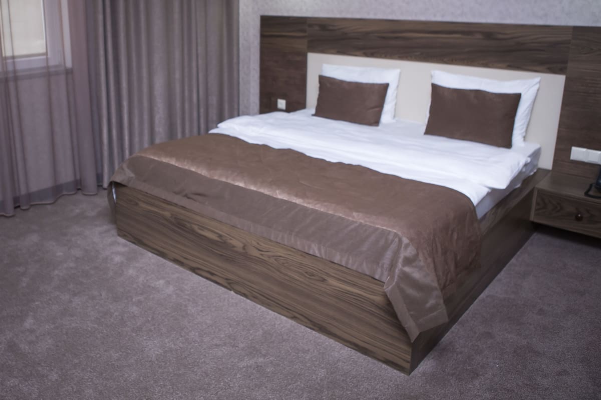 A neatly made bed with a wooden headboard, a bedside table, and a lamp on the wall.