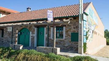 A stone building with a tiled roof, green doors, and a sign indicating it is a guesthouse.