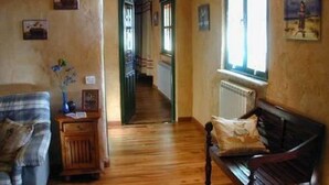 A cozy living room with a wooden floor, a sofa, a bench, and a window with artwork. - Hostería Casa Flor (Astorga)