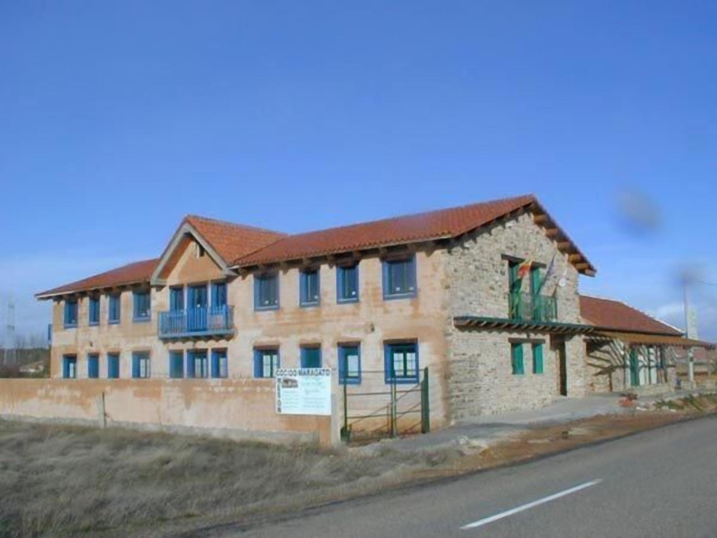 A two-story building with a stone facade, multiple windows, and a red-tiled roof.
