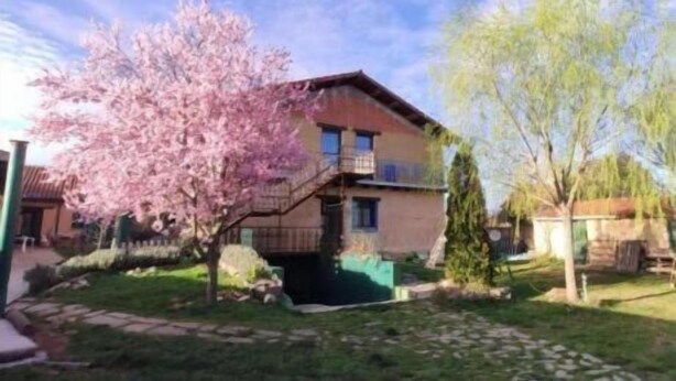 A two-story house with a balcony, surrounded by a garden with blooming trees. - Hostería Casa Flor (Astorga)